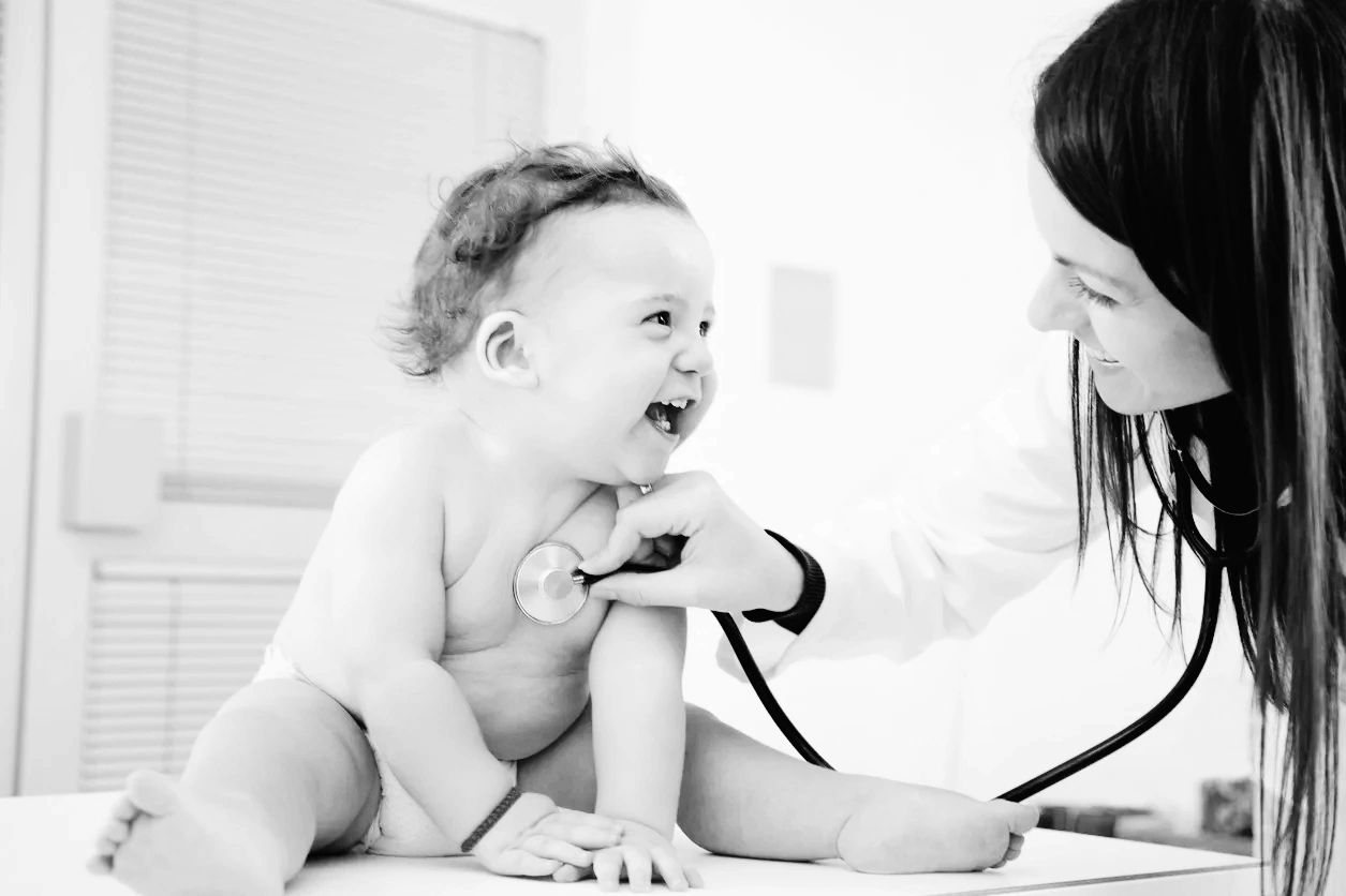 Pediatrician listening to a laughing infant’s chest with a stethoscope