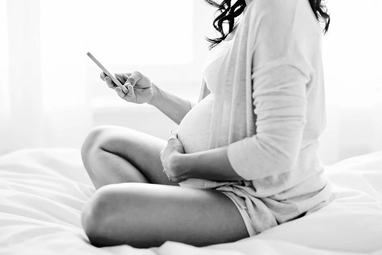 Pregnant woman sitting on a bed with a hand on her belly